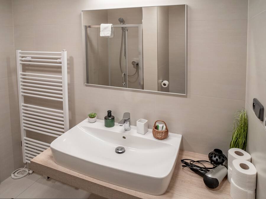 A modern bathroom with a white sink, a glass shower enclosure, a towel rack, and toiletries on the counter.