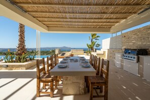 An outdoor dining area with a stone table and wooden chairs, overlooking a scenic view of the sea and mountains. - Villa Athena luxury Villa,Vamos,13.5/5m Swimming pool,floodlit Pickleball court (Vamos)