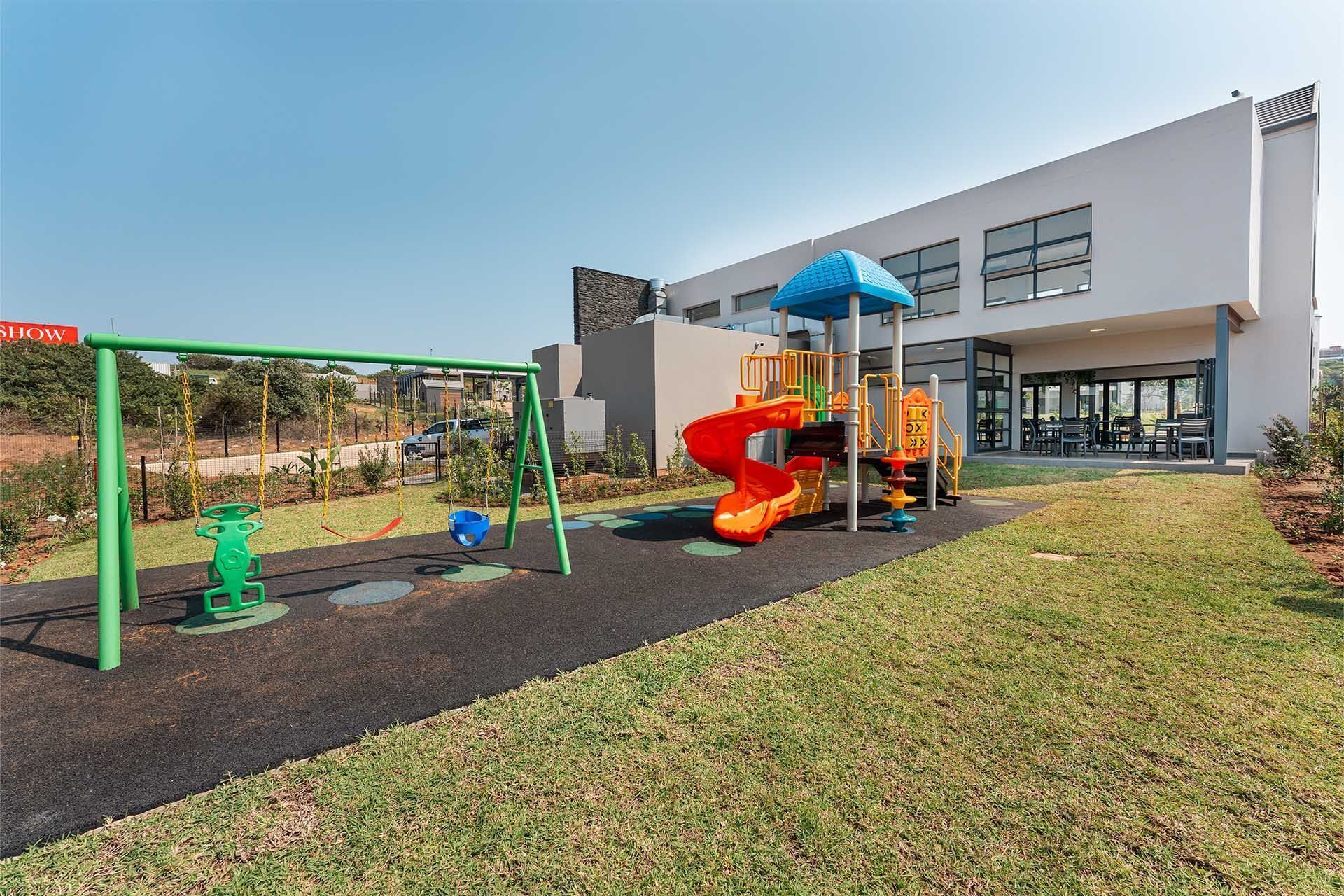 A playground with swings and slides, a grassy area, and a building with large windows.