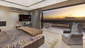 A modern bedroom with a large bed, a TV, and a balcony with a city view. - Baronetcy Kings Villa (Cape Town)