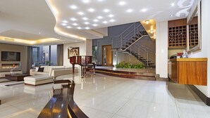 A spacious living area with a curved dark accent wall, a staircase, and a wine rack. - Baronetcy Kings Villa (Cape Town)