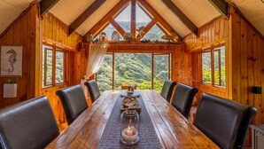 Ein Esszimmer aus Holz mit hoher Decke und großen Fenstern mit Blick auf einen Wald.