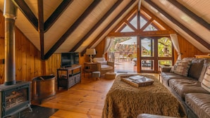 Ein gemütliches Dachzimmer mit Holzvertäfelung, einem Kamin, einem Fernseher und einer bequemen Sitzecke.