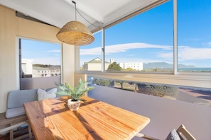 Una habitación con un ventanal grande, una mesa de madera, una lámpara de fibra natural y una planta en maceta.