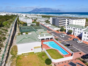 A residential area with a swimming pool, tennis courts, and a view of the ocean. - Big Bay Beach Club 37 (Cape Town)