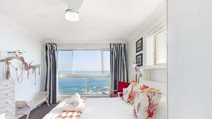 A bedroom with a large bed, a desk, and a view of the ocean.