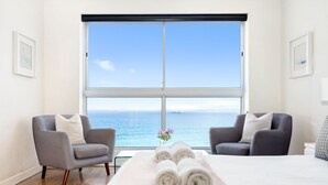A hotel room with a large window, two armchairs, a bed, and a small table with towels.