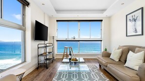 A modern living room with a large window overlooking the sea, a sofa, a coffee table, and a TV.