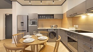 Une cuisine moderne avec un coin repas, des appareils en acier inoxydable, des chaises en bois et un lave-linge encastré.