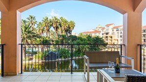 A balcony with a view of a water body, palm trees, and buildings in the background.