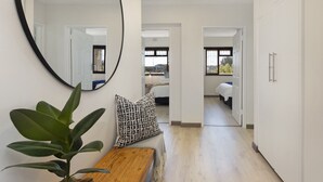 Un pasillo con un banco de madera, una planta en maceta y un espejo en la pared. Se observan puertas que dan a otras habitaciones.