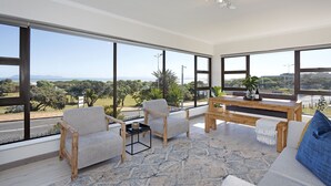 Amplia sala de estar con ventanas grandes, una mesa de centro de madera y un sofá con un cojín azul.