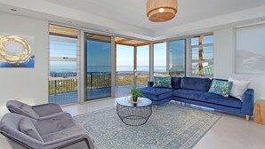 A modern living room with a blue sofa, a grey armchair, and a round coffee table with a plant. - Blueview on Silversand (Betty's Bay)