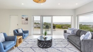 A modern living room with two sofas, a coffee table, and a large window with a view of the sea. - Blueview on Silversand (Betty's Bay)