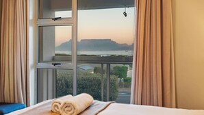 A hotel room with a large window, a bed with a rolled towel, and a view of a coastal landscape.