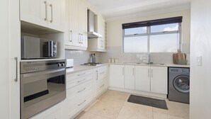 A modern kitchen with white cabinets, stainless steel appliances, and a large window. - Blouberg Heights 603 (Cape Town)
