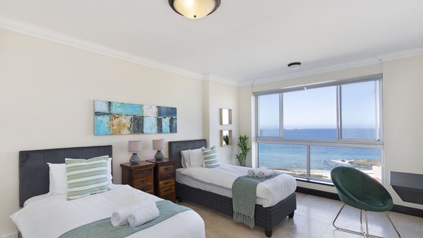 A hotel room with two beds, a view of the ocean, and a green chair. - Blouberg Heights 603 (Cape Town)