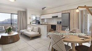 A modern living room with a sofa, a dining table set for four, and a kitchen area with a refrigerator and stove.