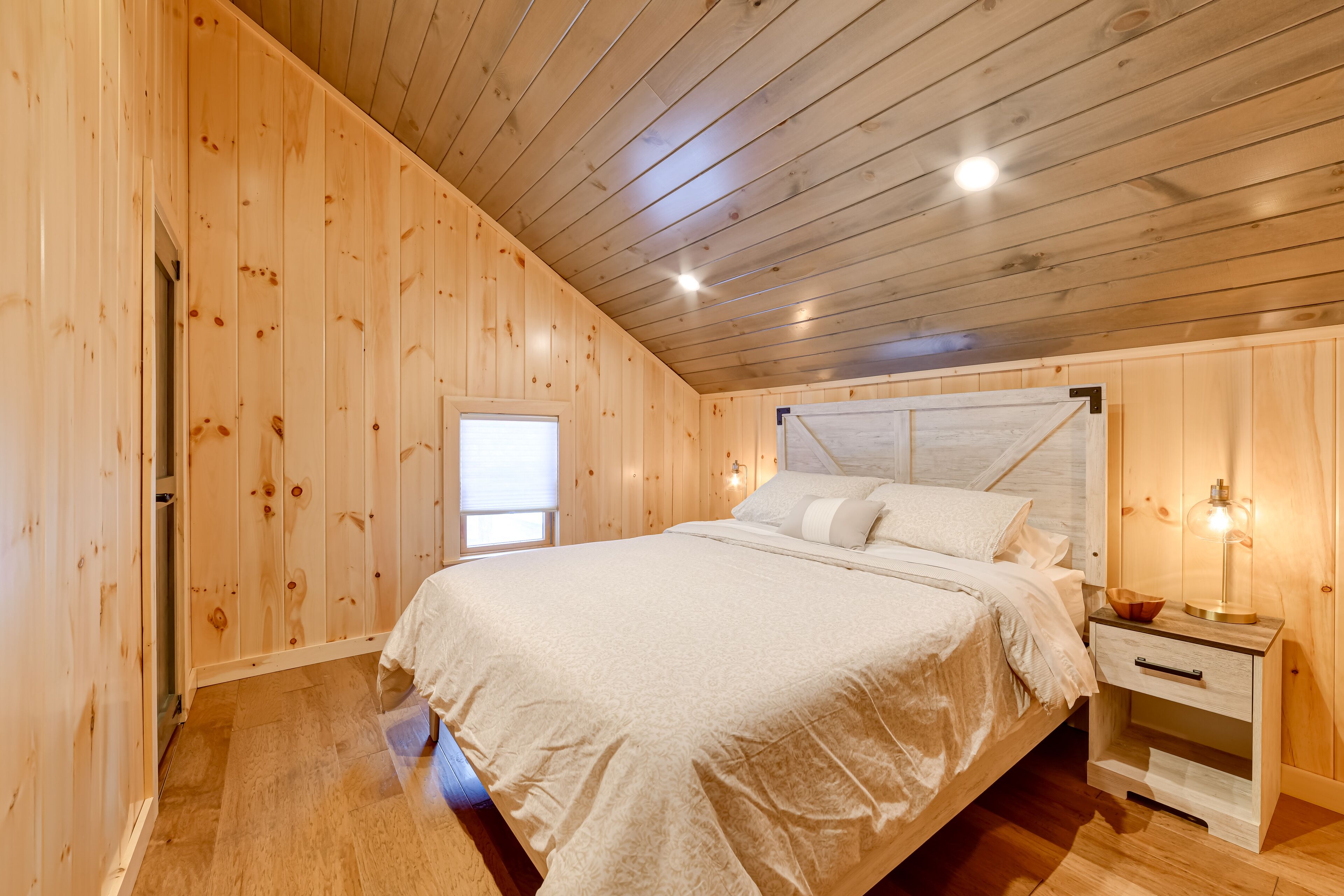 A wooden-paneled bedroom with a bed, bedside table, and a window.
