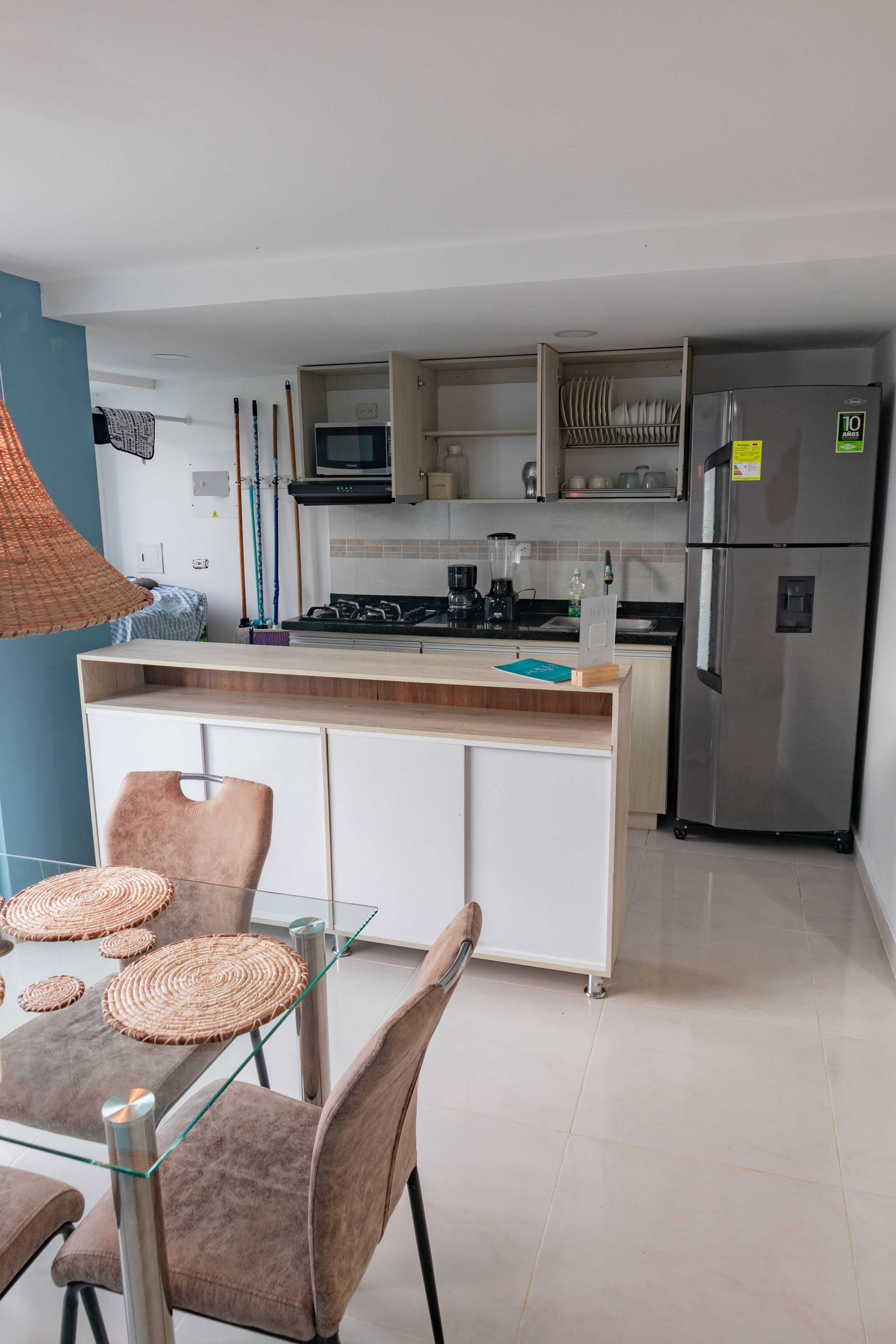 A modern kitchen with a central island, stainless steel appliances, and a dining area with glass tables and chairs.