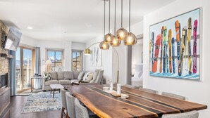 A spacious dining area with a long wooden table, grey upholstered chairs, and a modern pendant light fixture.