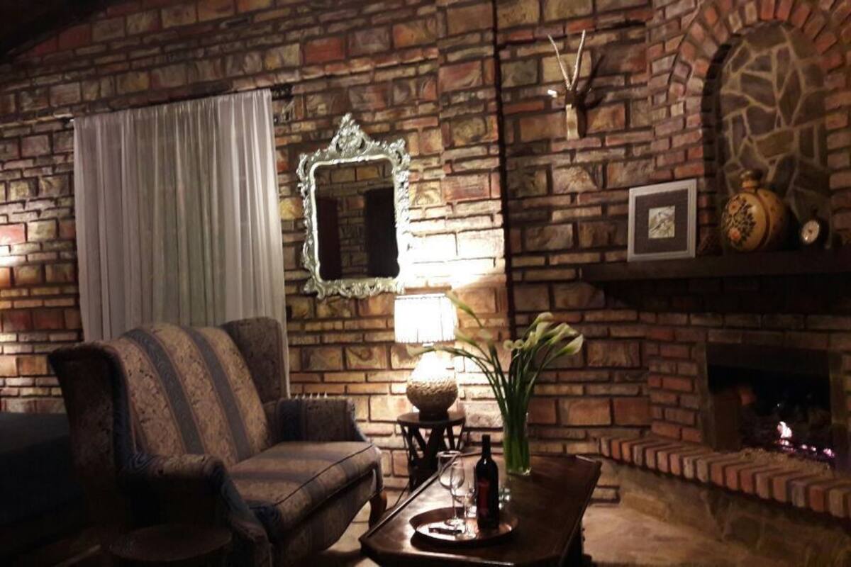 A cozy room with a brick fireplace, a sofa, a coffee table with a vase and wine bottle, and a mirror on the wall.