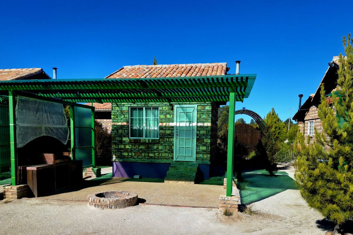 A traditional wooden house with a tiled roof, a green porch, and a brick fire pit.