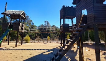 Un parque infantil con un puente de cuerdas, estructuras de madera para escalar y un tobogán.