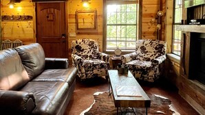 Ein gemütliches Blockhaus-Interieur mit einer Ledersofa, zwei gemusterten Sesseln, einem Holztisch und einem Kamin.