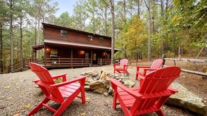 Eine Holzhütte mit Terrasse, roten Adirondack-Stühlen und einem Feuerkorb.