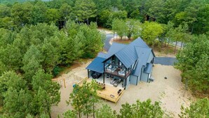 Una casa moderna de dos pisos con un amplio balcón y zona de estar exterior, rodeada de un bosque denso.