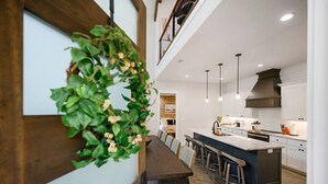 Una cocina moderna con una isla central, iluminación colgante y una escalera de madera.