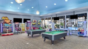 Ein Poolbereich mit zwei Billardtischen, Spielautomaten und einem großen Fenster mit Blick auf einen Pool.