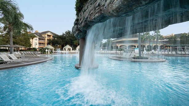 Ein Pool mit Wasserfall, Liegestühlen und einem Gebäude im Hintergrund.