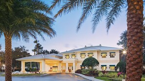 Ein Hotel mit zwei Etagen, einem überdachten Eingang, Palmen und gepflegten Gärten.