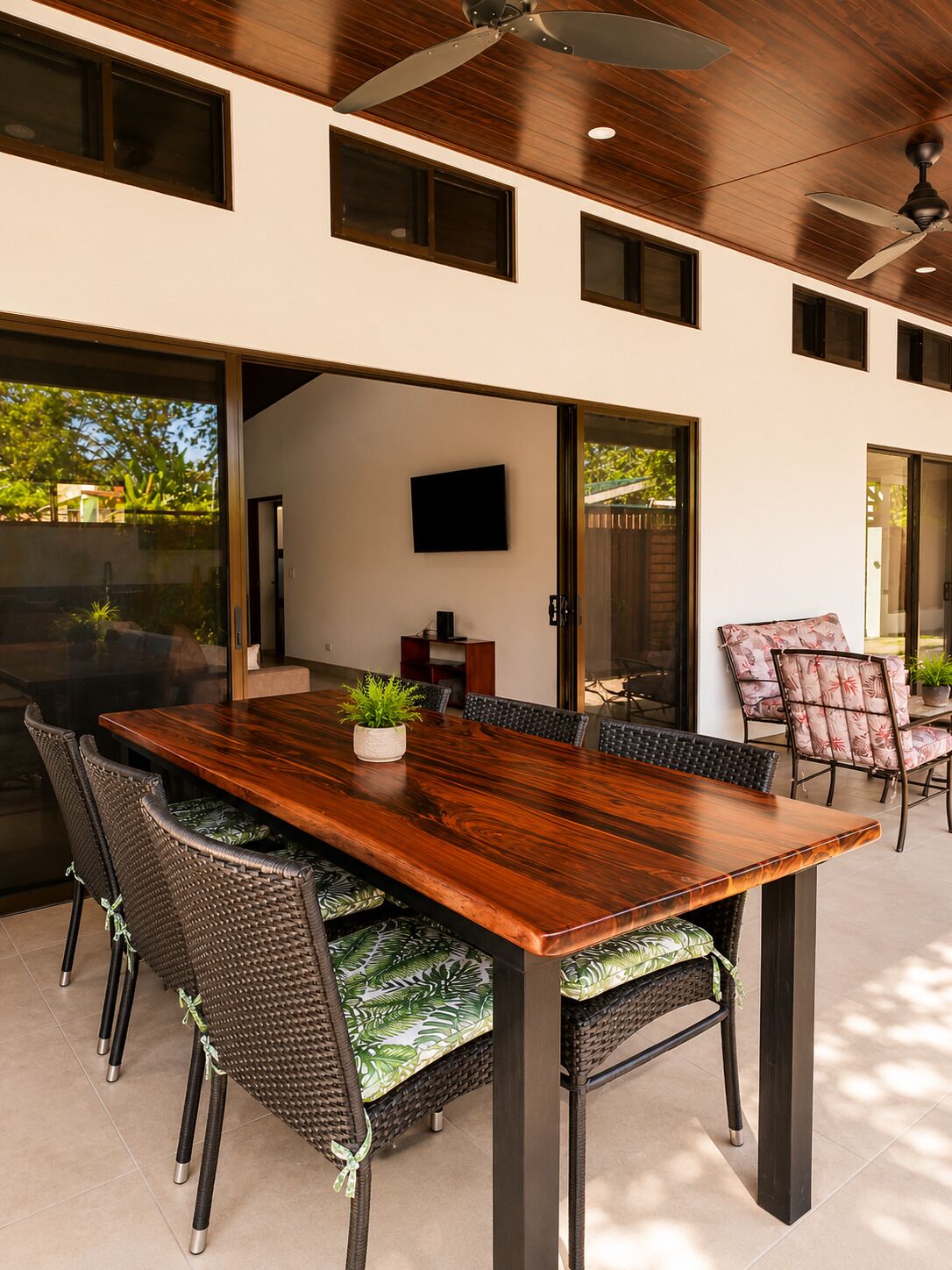 Un coin repas avec une table en bois et des chaises en osier, un téléviseur fixé au mur et un ventilateur de plafond.