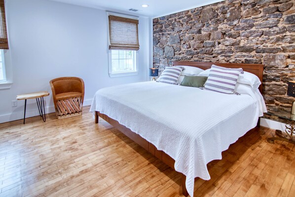 A bedroom with a large bed, a wooden floor, a stone wall, and a chair.