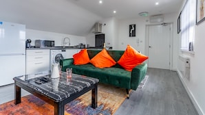 A compact living space with a kitchenette, a green sofa with orange cushions, a marble coffee table, and a colorful rug. - Birmingham Apt-sleeps 4-walk to City Centre-pets (Birmingham)