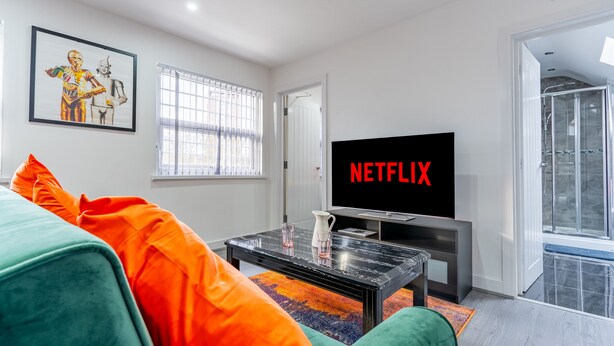 A modern living room with a large flat-screen TV displaying "NETFLIX", a colorful rug, and vibrant cushions. - Birmingham Apt-sleeps 4-walk to City Centre-pets (Birmingham)