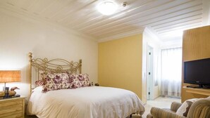 A hotel room with a bed, a nightstand, a television, and a striped armchair. - Pousada Casa Gialla - Campos do Jordão (Campos do Jordão)