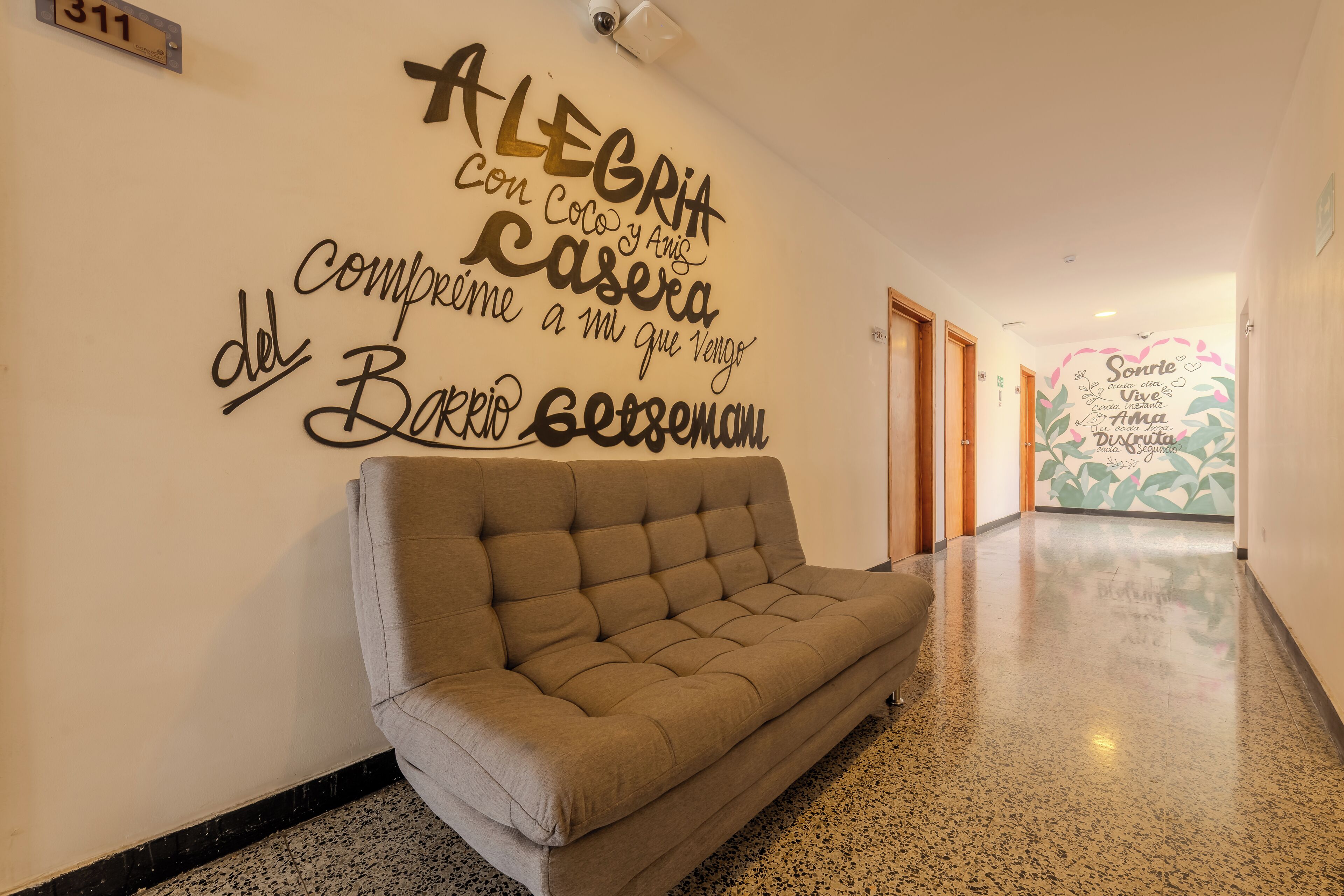 Un pasillo con un sofá, una pared con texto motivacional y una puerta al final.