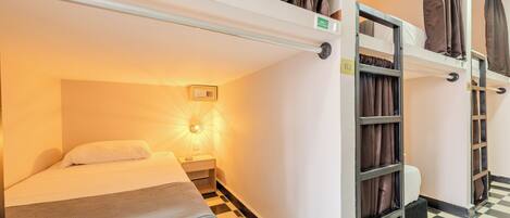 A bunk bed room with a checkered floor, a bedside table with a lamp, and a window with curtains.