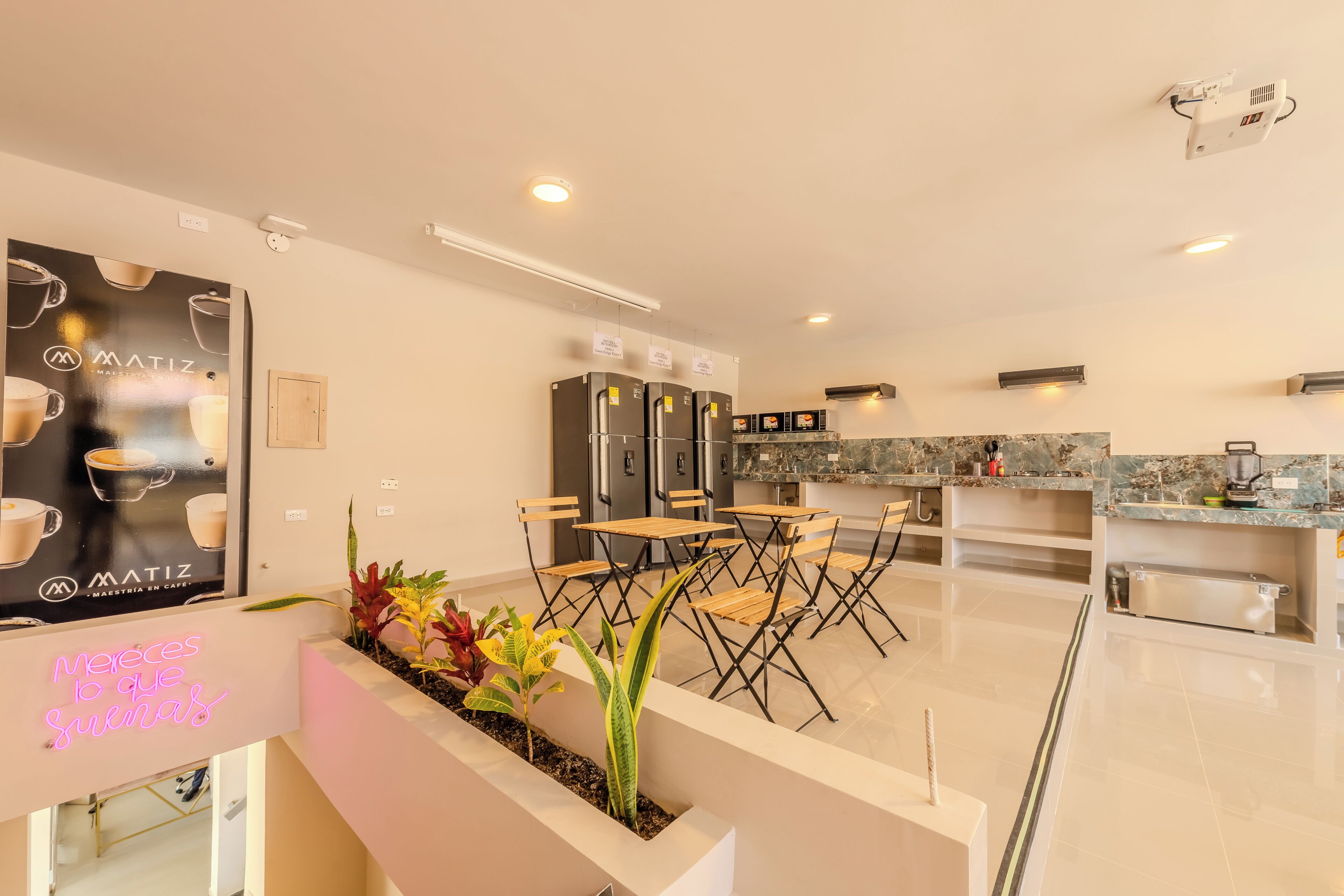 A modern kitchen with stainless steel appliances, a dining area with foldable chairs, and a neon sign.
