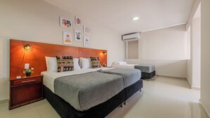 Une chambre d’hôtel moderne avec un grand lit, des tables de chevet, une commode et un climatiseur fixé au mur.
