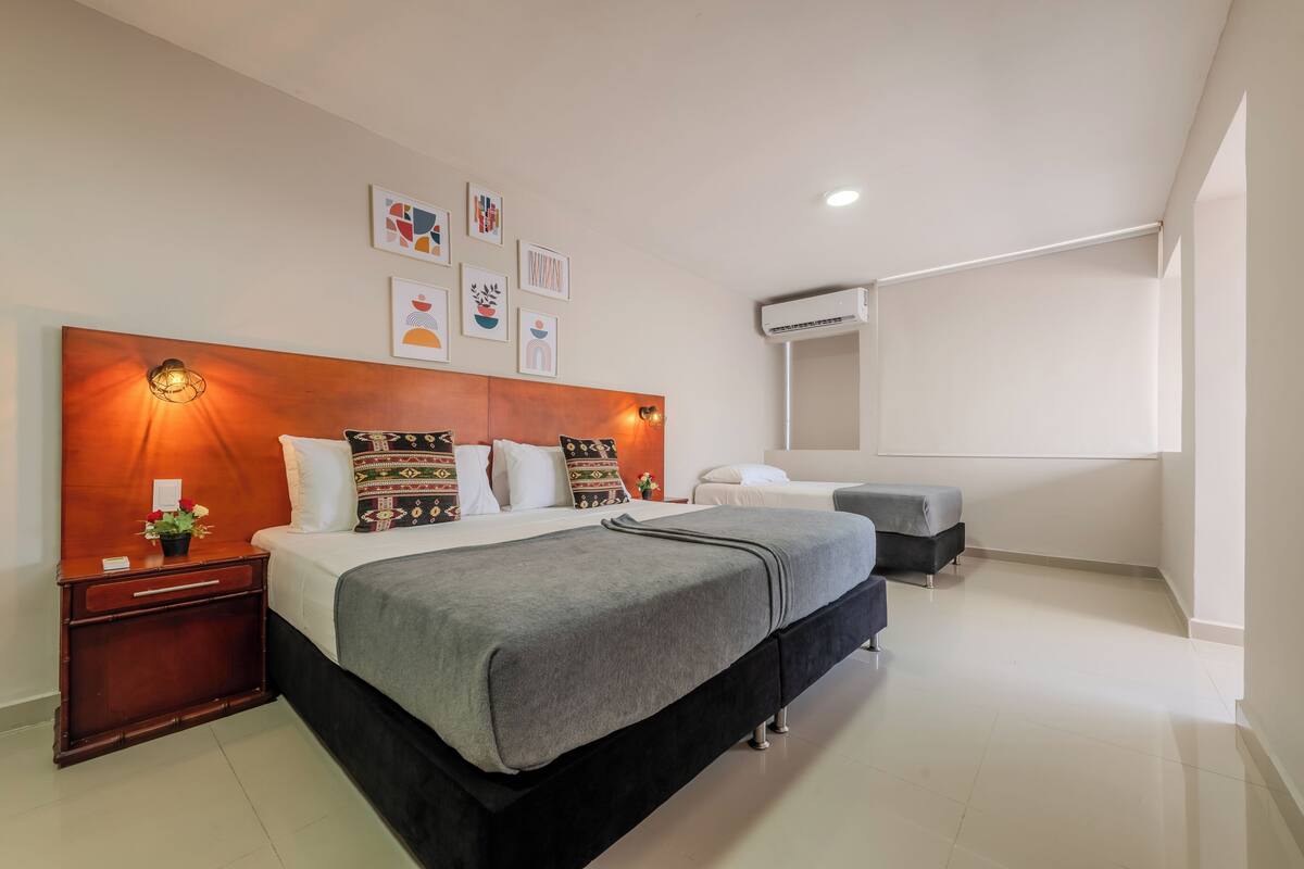 A modern hotel room with a large bed, bedside tables, a dresser, and a wall-mounted air conditioning unit.