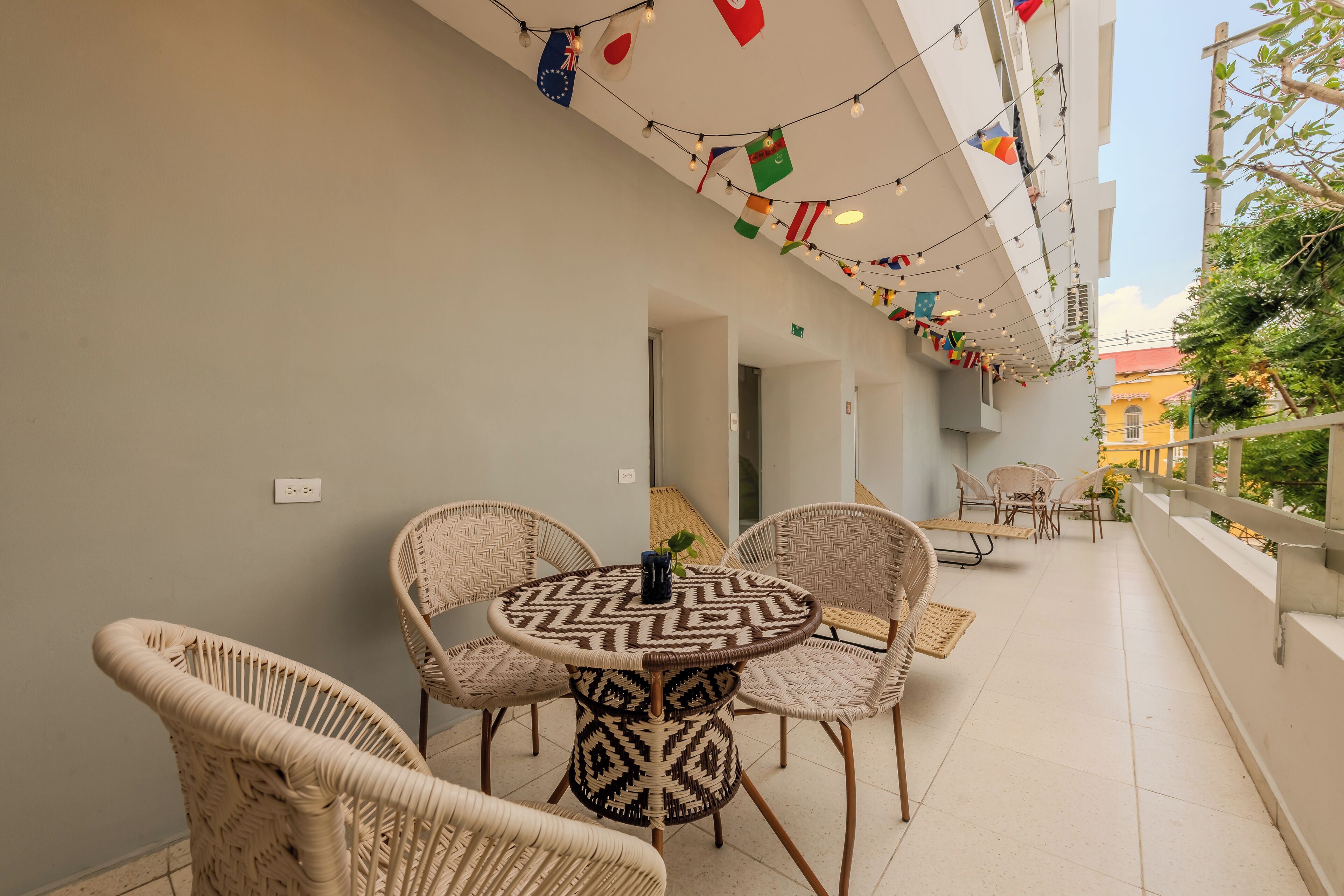 Un balcon agrémenté de meubles en osier, d’une table à motifs et de guirlandes lumineuses.