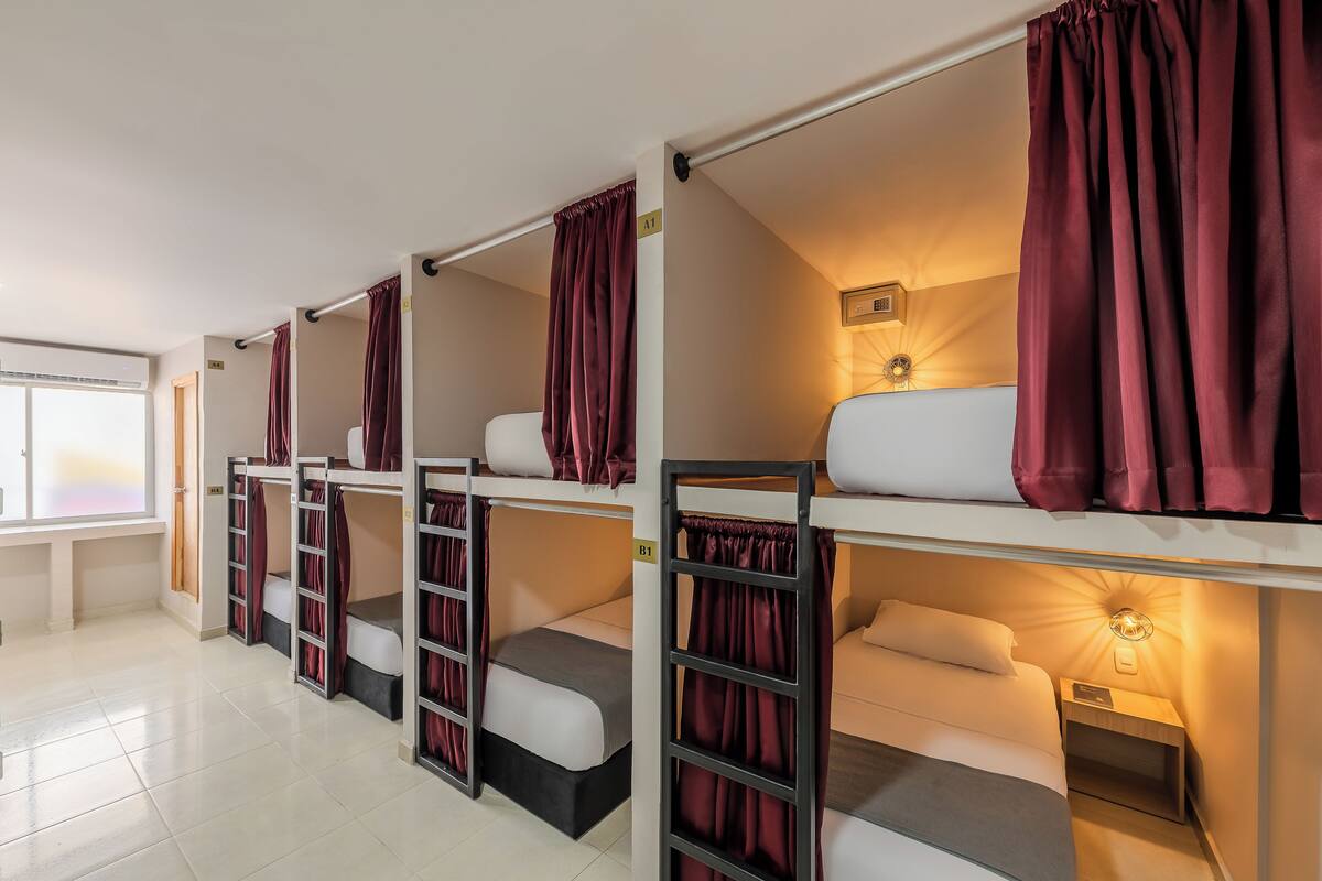 A dormitory room with bunk beds, a window, and a wall-mounted light fixture.