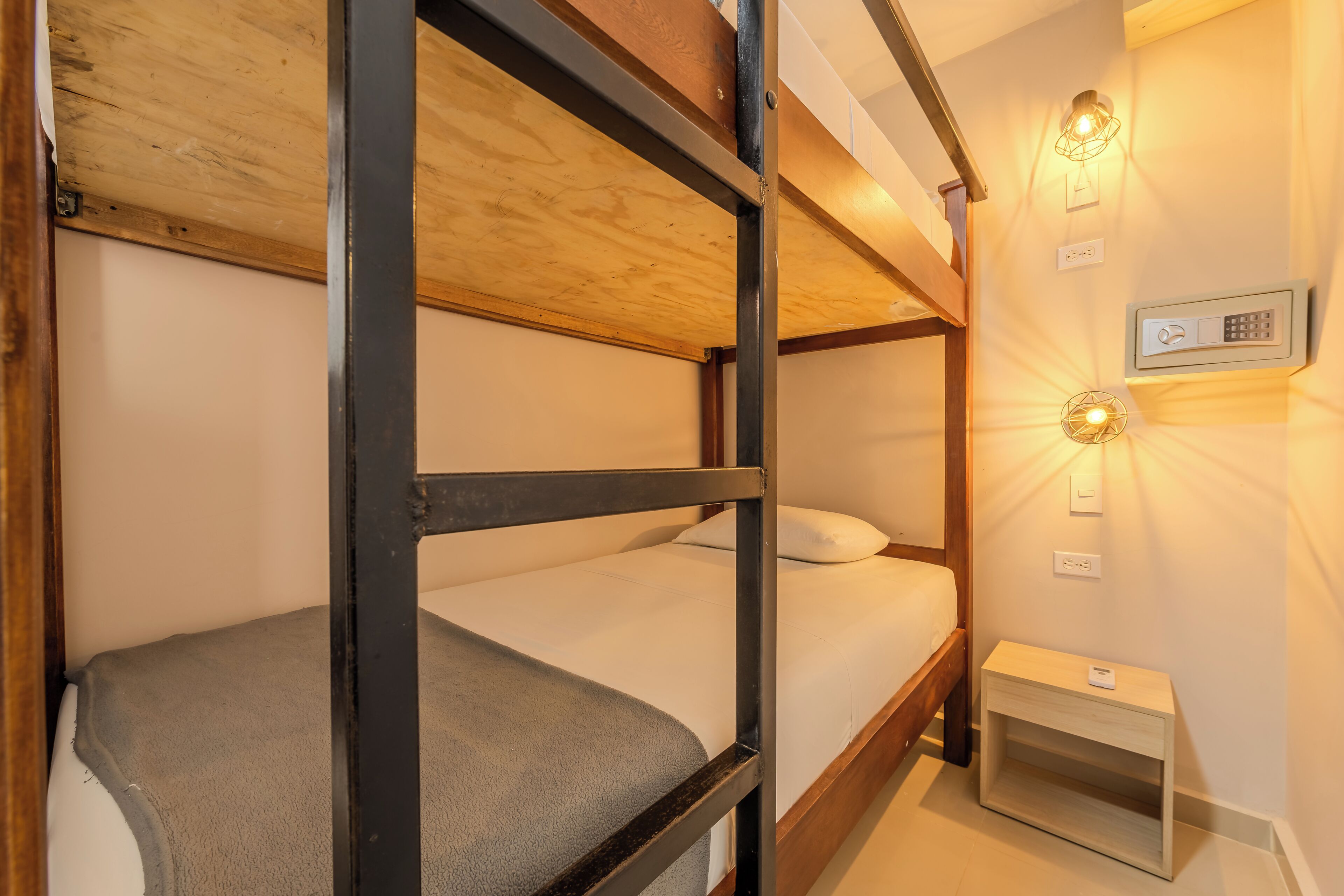 Une chambre avec des lits superposés, dotée d’un panneau de commande et d’un luminaire fixé au mur.