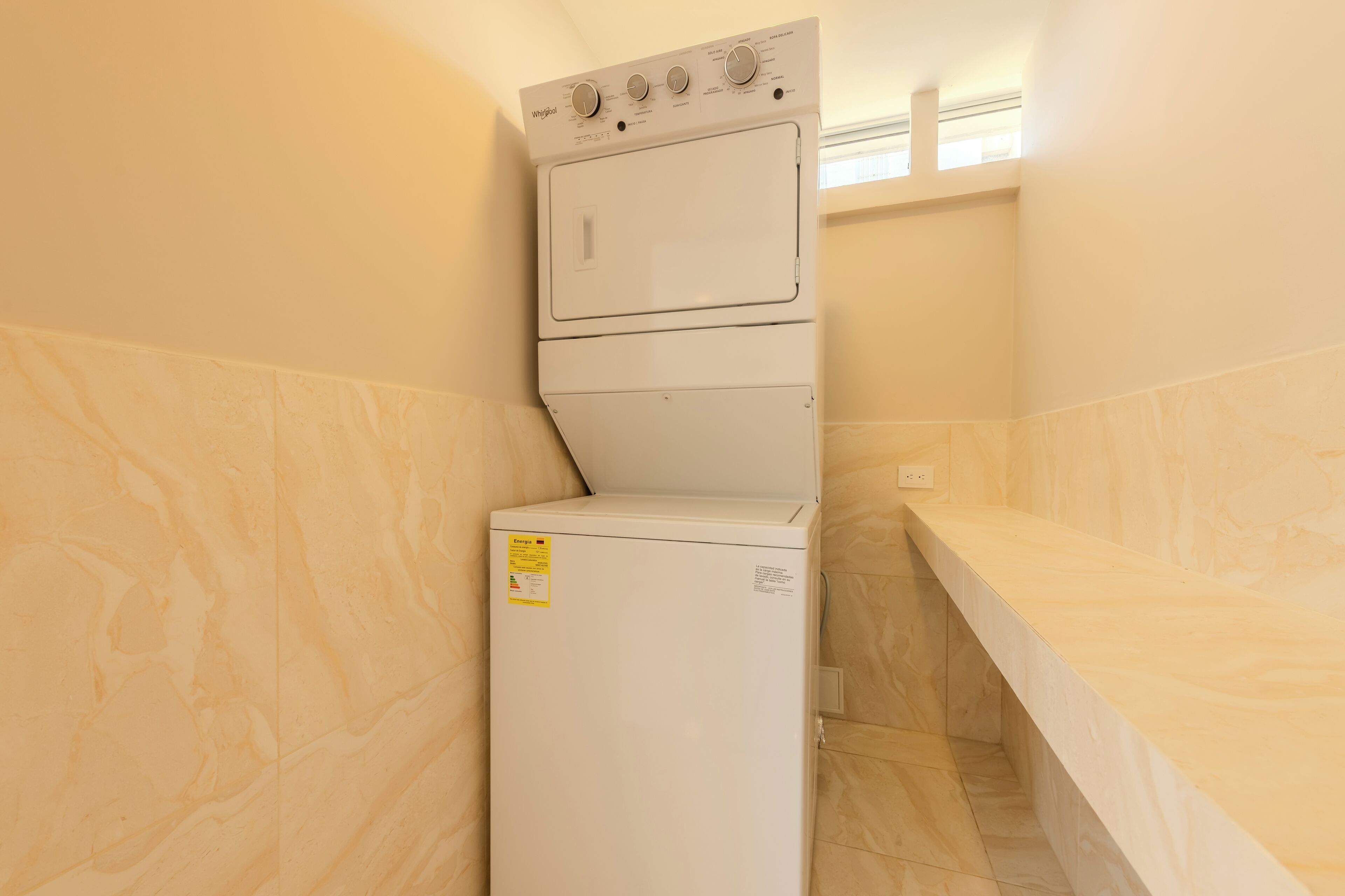 A compact laundry room with a front-loading washer and dryer, a marble-tiled wall, and a countertop.