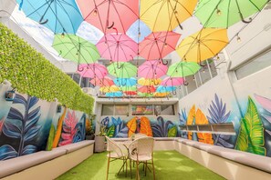 A room with a ceiling decorated with colorful umbrellas, a wall mural of leaves, and a small seating area with chairs. - Hostel Dorado Plaza Getsemaní (Cartagena)